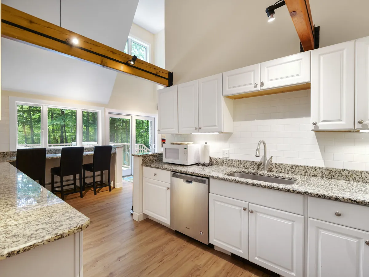 A modern kitchen with granite countertops, state-of-the-art appliances, and large windows offering outdoor views. Wooden beam accents add warmth to the functional space designed for cooking and entertaining.