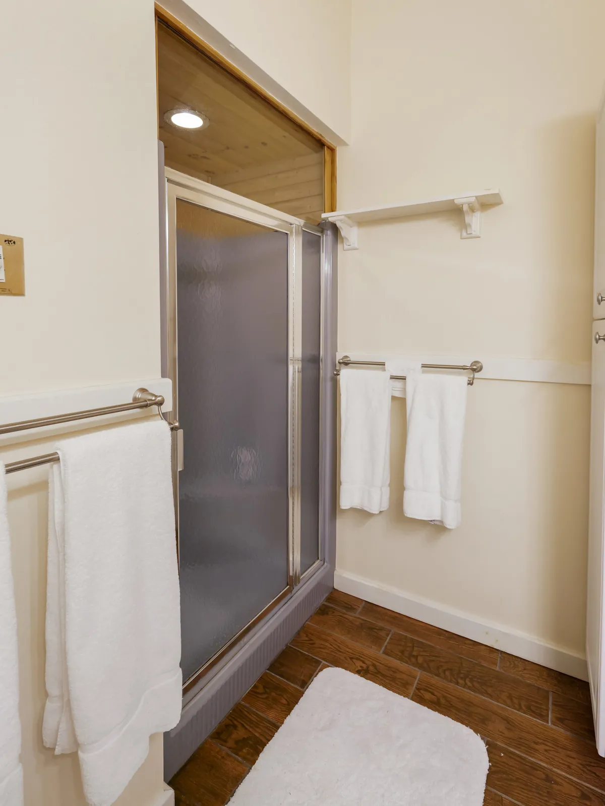 A modern bathroom with a glass-enclosed steam shower, fluffy white towels, and warm wooden floors. The space emanates cleanliness and a calming, inviting atmosphere perfect for self-care routines.