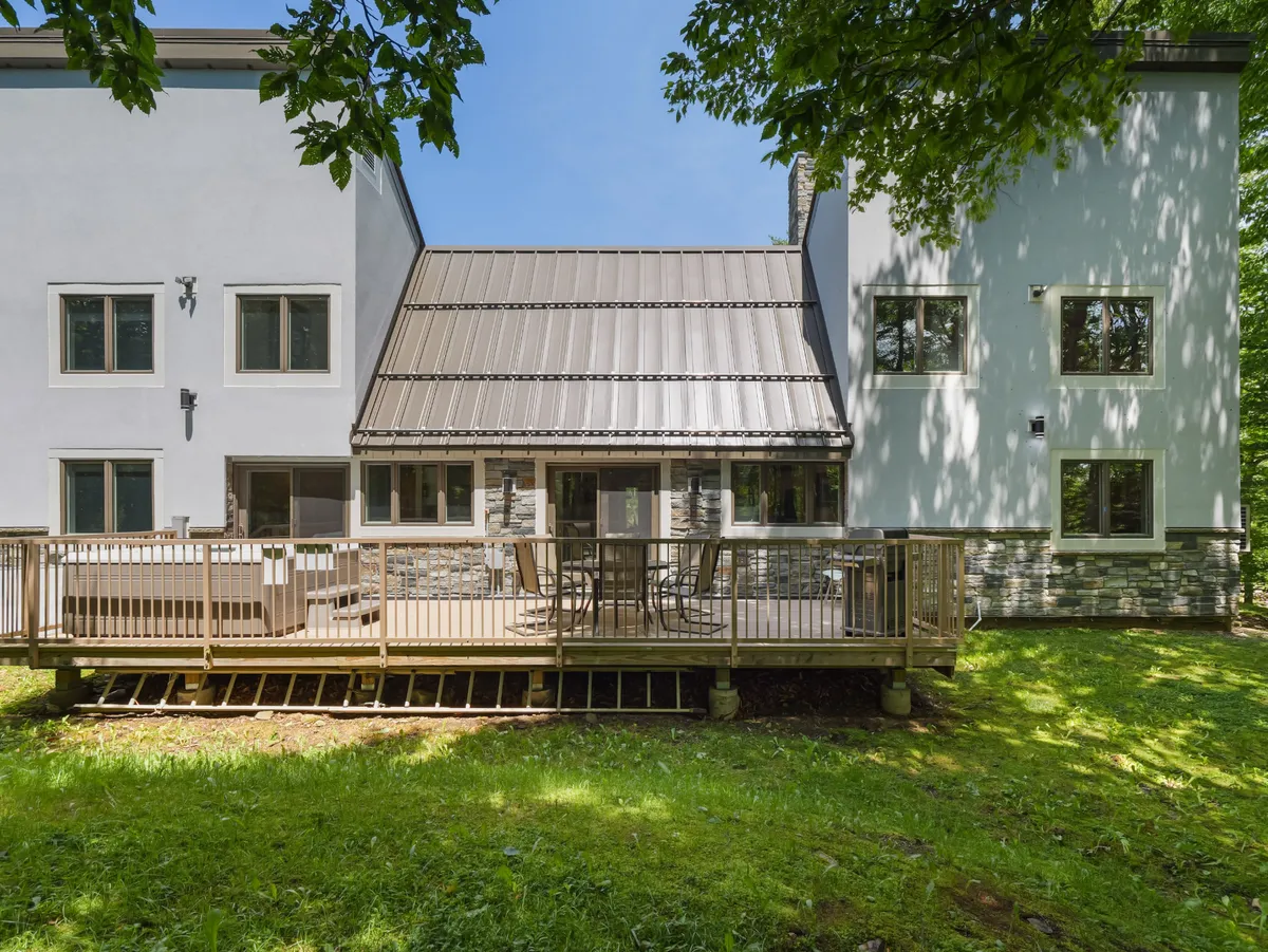 This exterior shot captures the deck area with large windows and stone accents, offering ample space for outdoor relaxation and dining while enjoying tranquil views of the surrounding landscape.
