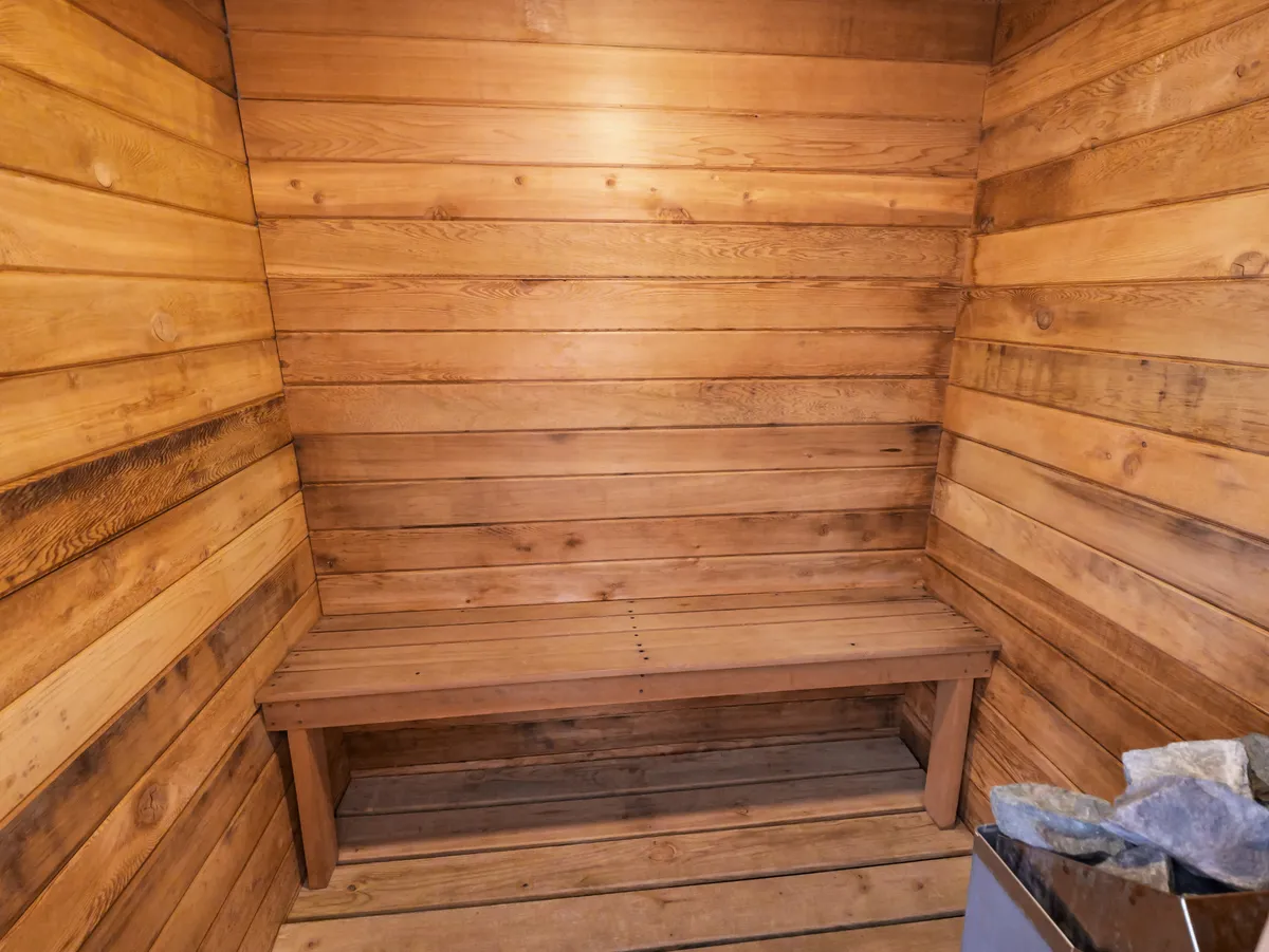 A warm and tranquil cedar sauna interior with wooden benches and walls, and a pile of stones ready to heat the space. The mood is peaceful, suggesting rejuvenation and recovery after outdoor activities.