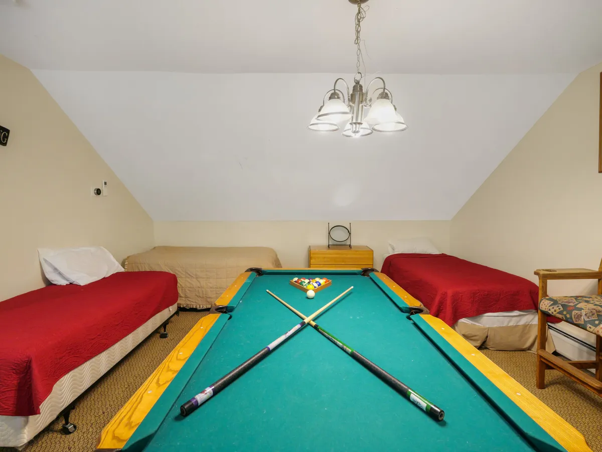 A friendly, relaxed interior with a pool table as the centerpiece, flanked by beds and illuminated by a stylish light fixture. The setting invites late-night games, conversations, and bonding in a casual environment.