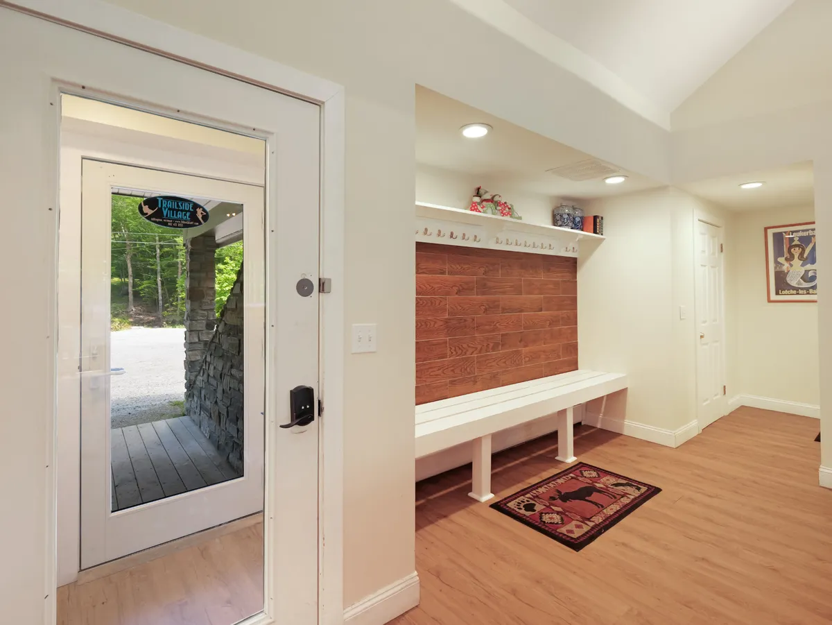 This image captures the front door area with a wooden bench, accent rug, and wall paneling, highlighting the intimate, welcoming moment as guests enter the home. The natural wood and soft lighting evoke comfort and warmth, setting the tone for a luxurious and restorative stay.