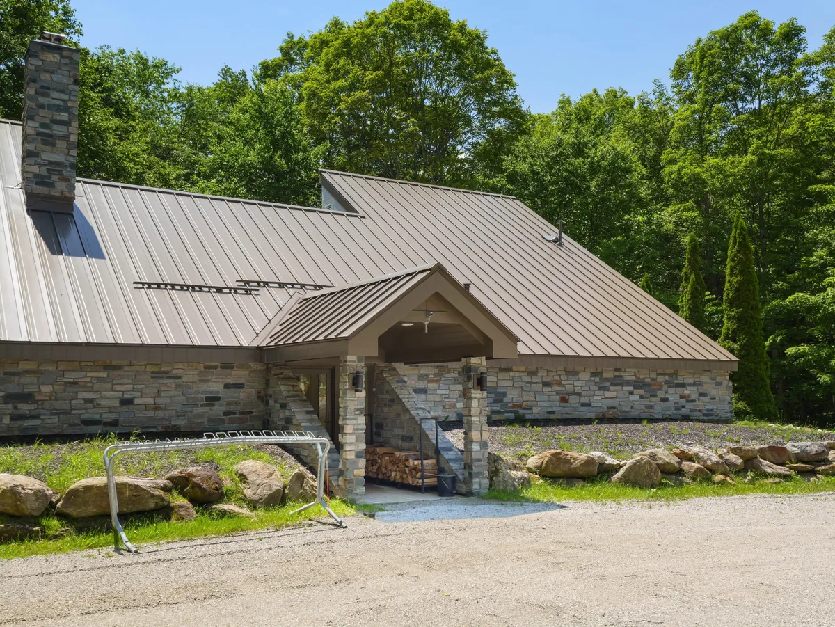 This exterior shot captures the home's stone facade, metal roof, wooden steps, and lush greenery. The welcoming porch area hints at pet-friendly and family gatherings, with natural surroundings inviting kids and pets to explore safely.