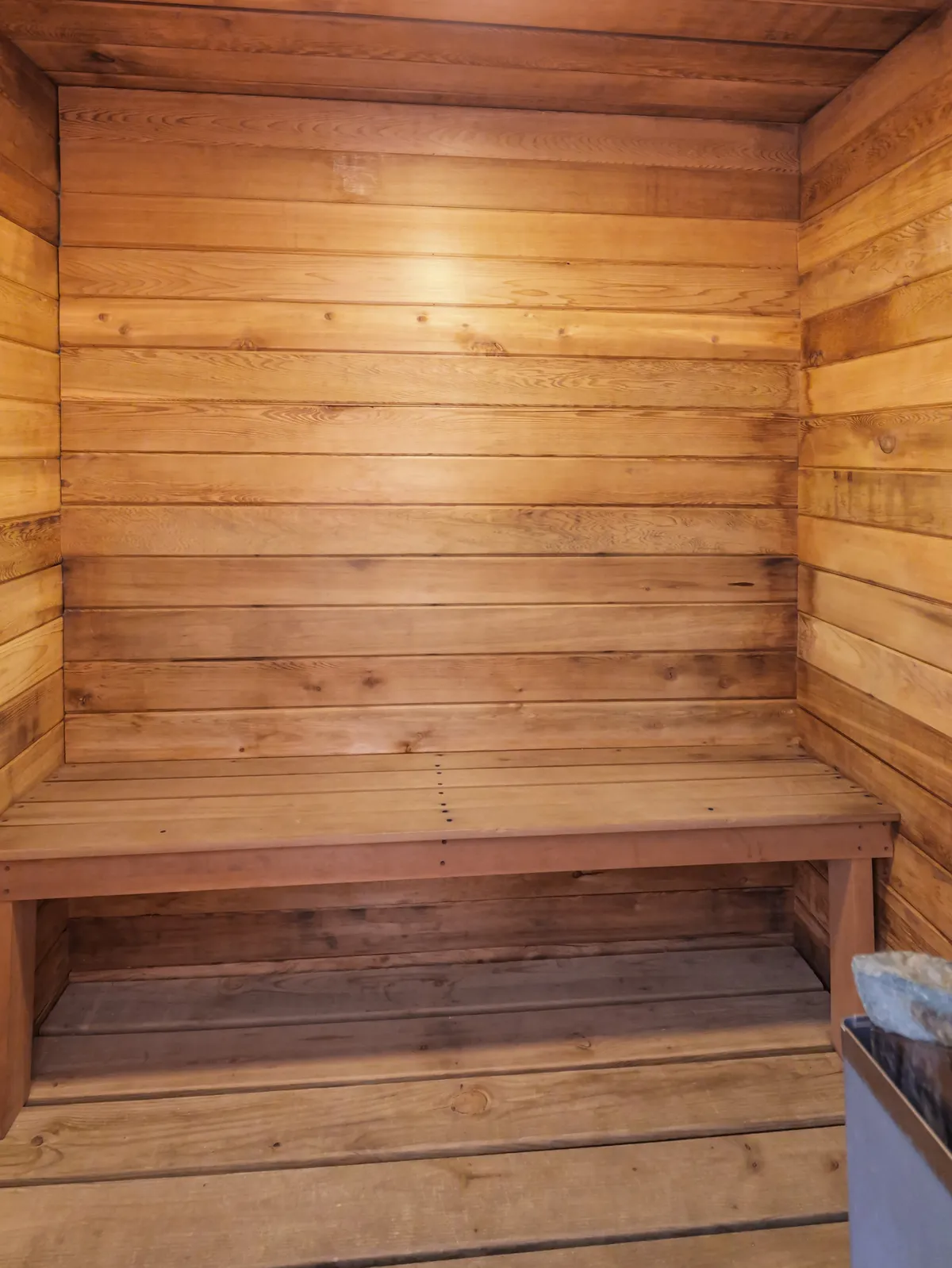 A calming interior view of a cedar sauna, featuring wooden bench seating and a stone heater. The inviting, warm wood tones convey a spa-like environment ideal for relaxation after outdoor adventures.