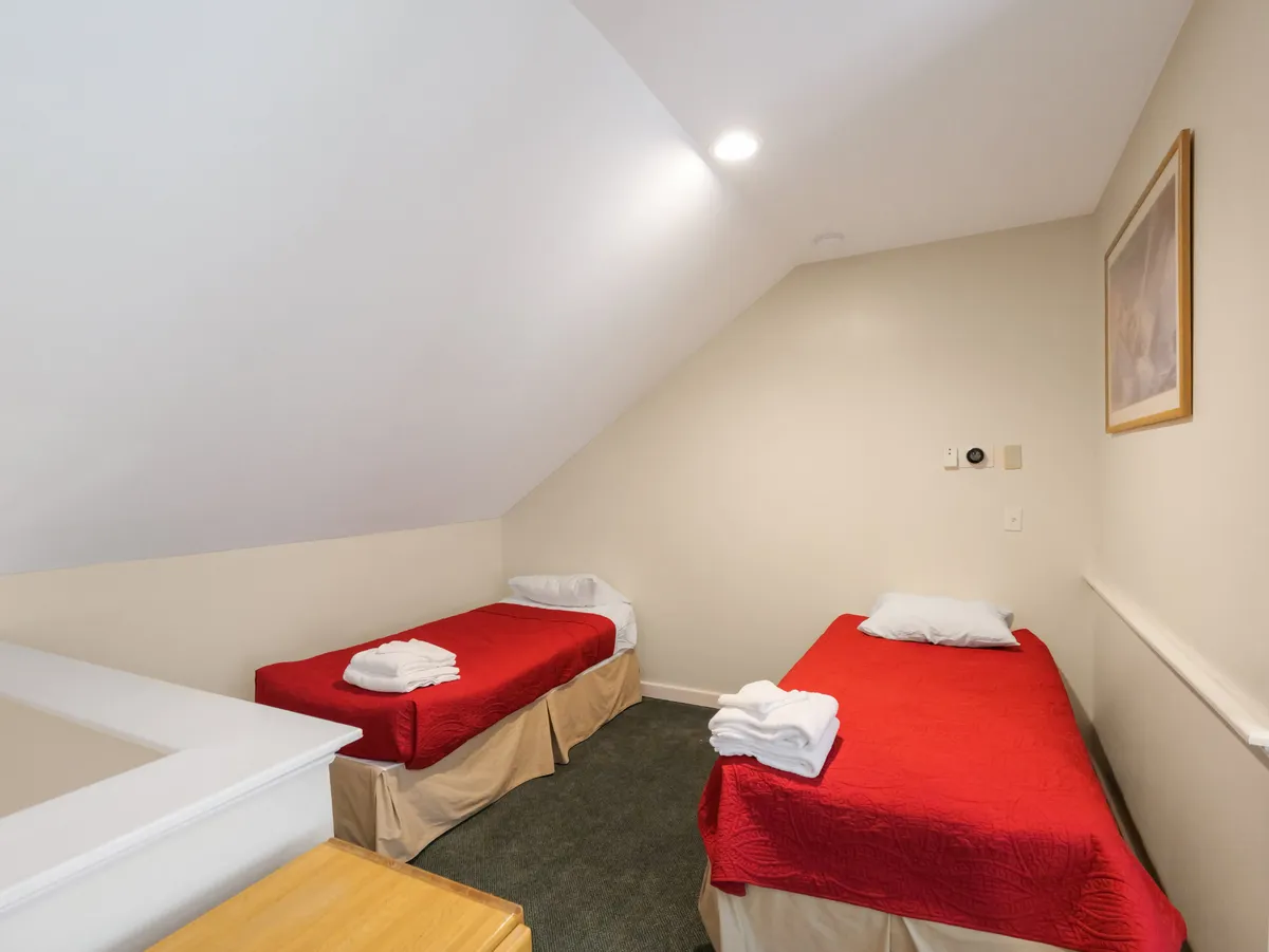 A welcoming bedroom featuring two beds with red bedspreads, neatly placed white towels, and framed art on the wall. The ambiance is warm and inviting, suggesting a space designed for relaxation and comfort.