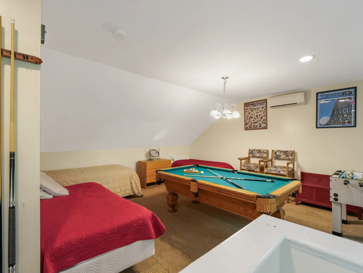 A multi-purpose entertainment space with a pool table, foosball table, armchairs for relaxing, and a bed in the background. The scene conveys a casual, inviting atmosphere ideal for both games and unwinding after a long day.