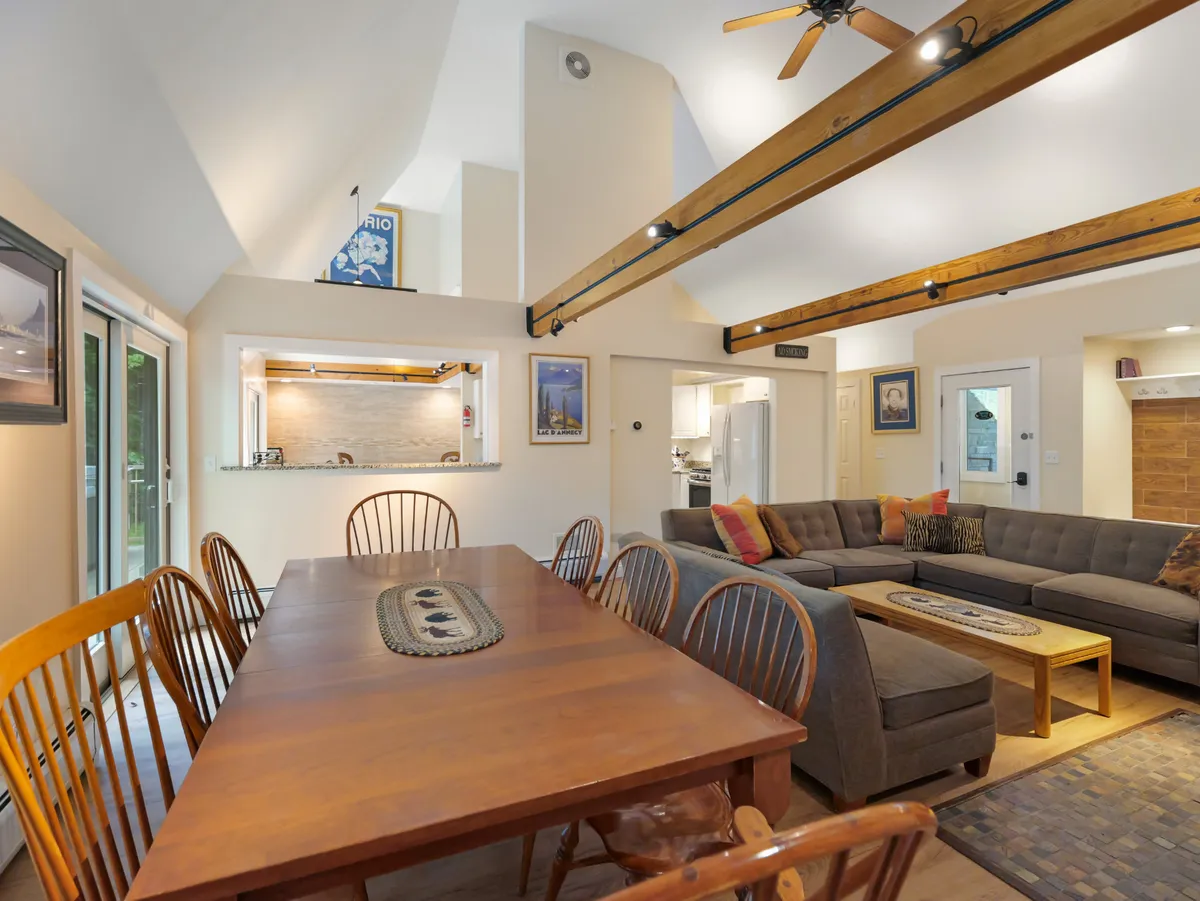 A welcoming scene showcasing a large dining table, comfortable sectional sofa, and an open kitchen area in a seamless layout. The space feels bright and communal, ideal for group meals and socializing.